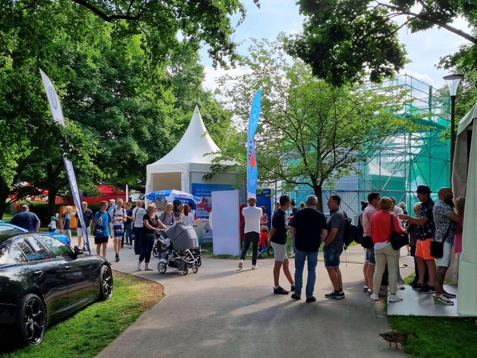 Auf diesem Bild sehen Sie viele Messebesucher/innen, die bei schönem Wetter durch den Hofgarten laufen und sich Messestände ansehen