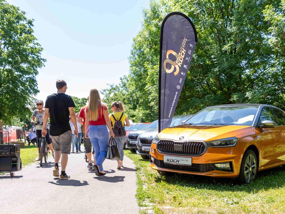 Auf diesem Bild sehen Sie Messebesucher/innen, die über einen Fußweg das Messegelände besuchen und sich Autos ansehen.